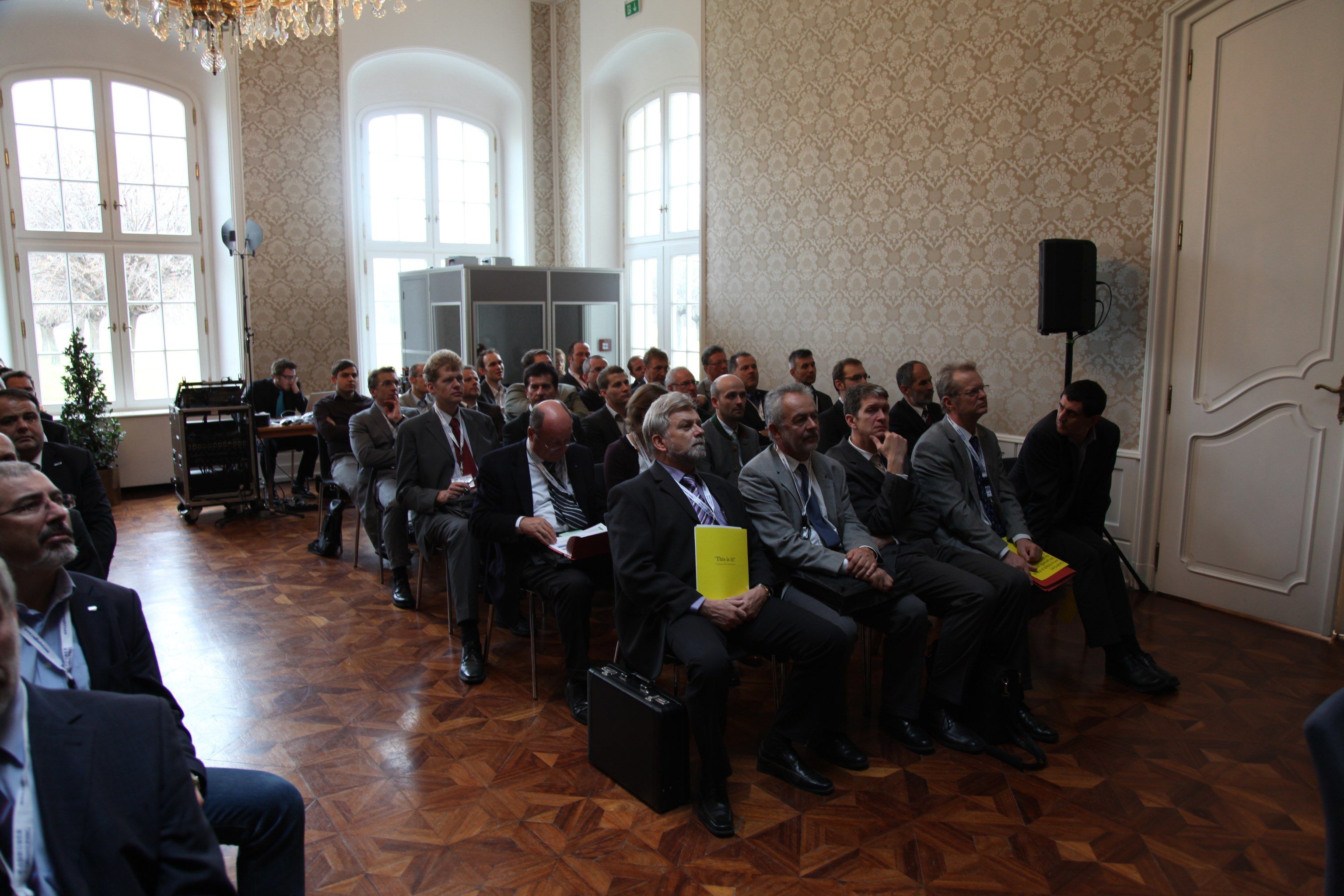 Blick über den voll besetzten Saal mit Parkettboden und hohen Fenstern.